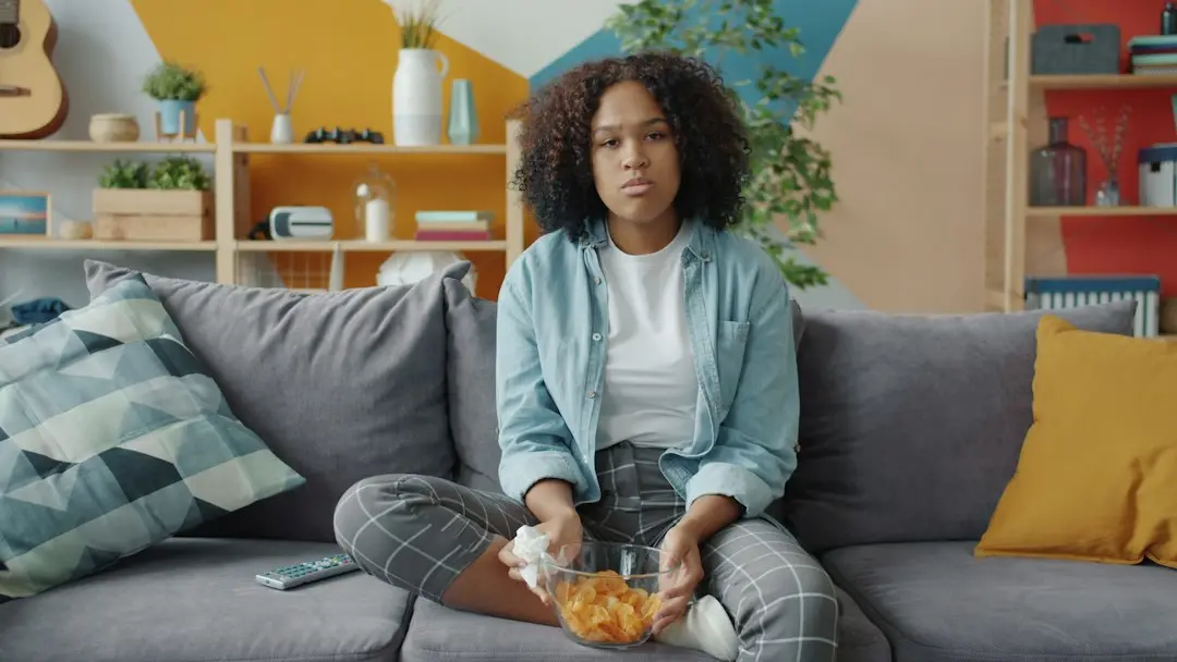 Una mujer sentada en el sofá con un bol de patatas y el mando a distancia, lista para ver IPTV Fiesta