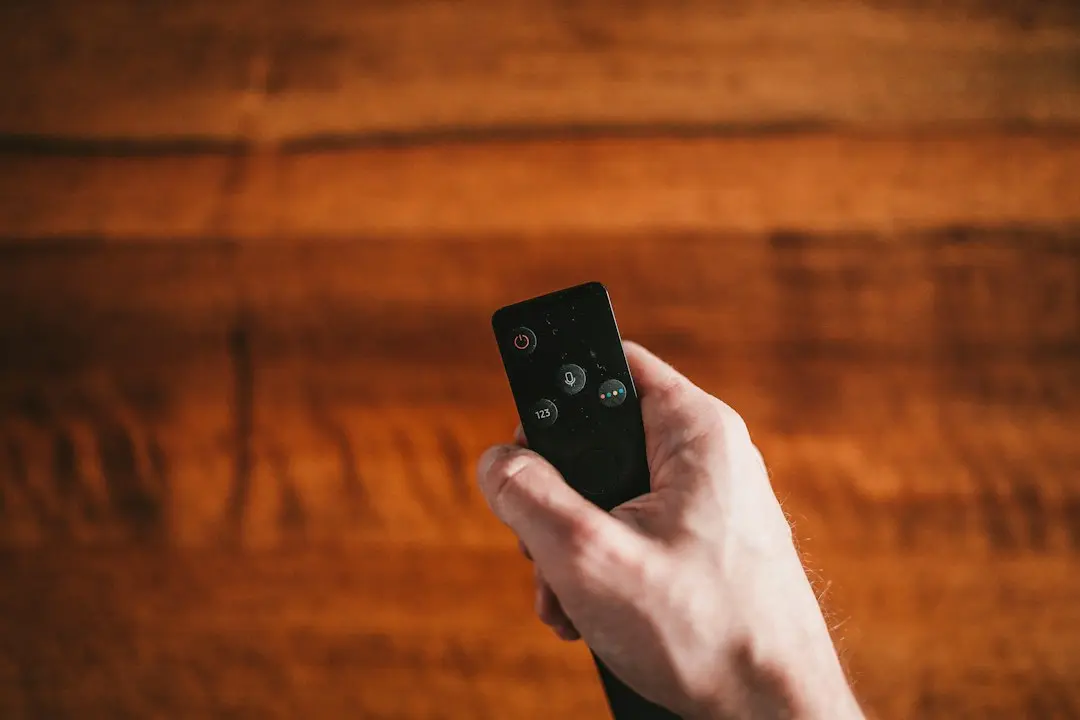 Una mano sostiene un mando a distancia sobre un fondo de madera, lista para configurar IPTV Fiesta